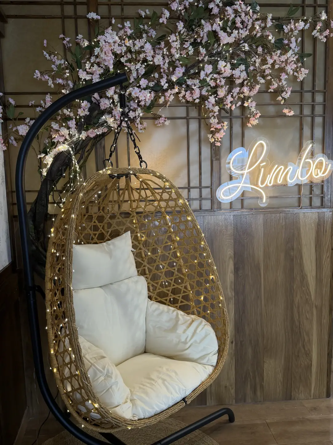 Interior de Limbo: silla colgante bajo un cerezo en flor con luces y el neón Limbo